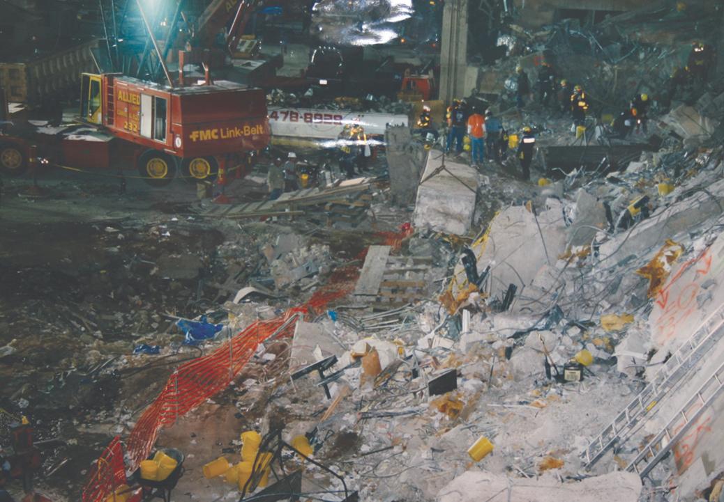 Foto de equipes e veículos de emergência cercando o local da detonação, em meio aos escombros.