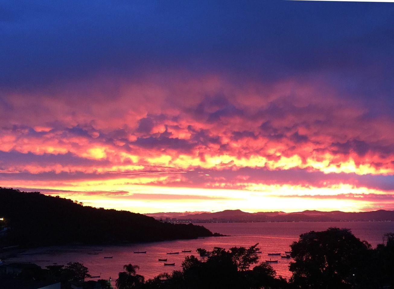 Vista de um por do sol avermelhado sobre o porto de pescadores do bairro João Paulo, em Florianópolis<br>