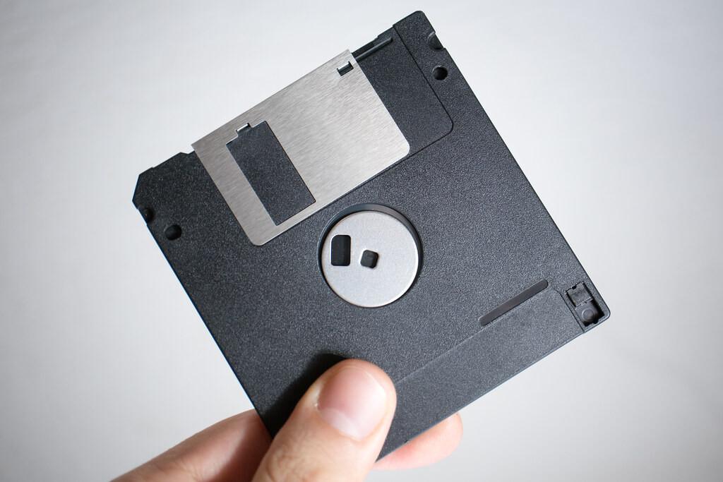 Foto de um disquete de 3,5 polegadas sendo segurado pela mão de uma pessoa