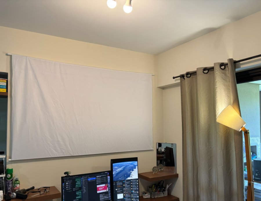 Foto de uma tela de tecido branco ocupando toda a parede acima dos 2 monitores do meu escritório.