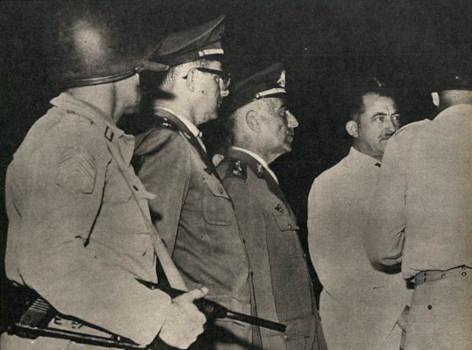 Foto em preto e branco do momento em que Miguel Arraes interage com os oficiais enviados para prendê-lo.