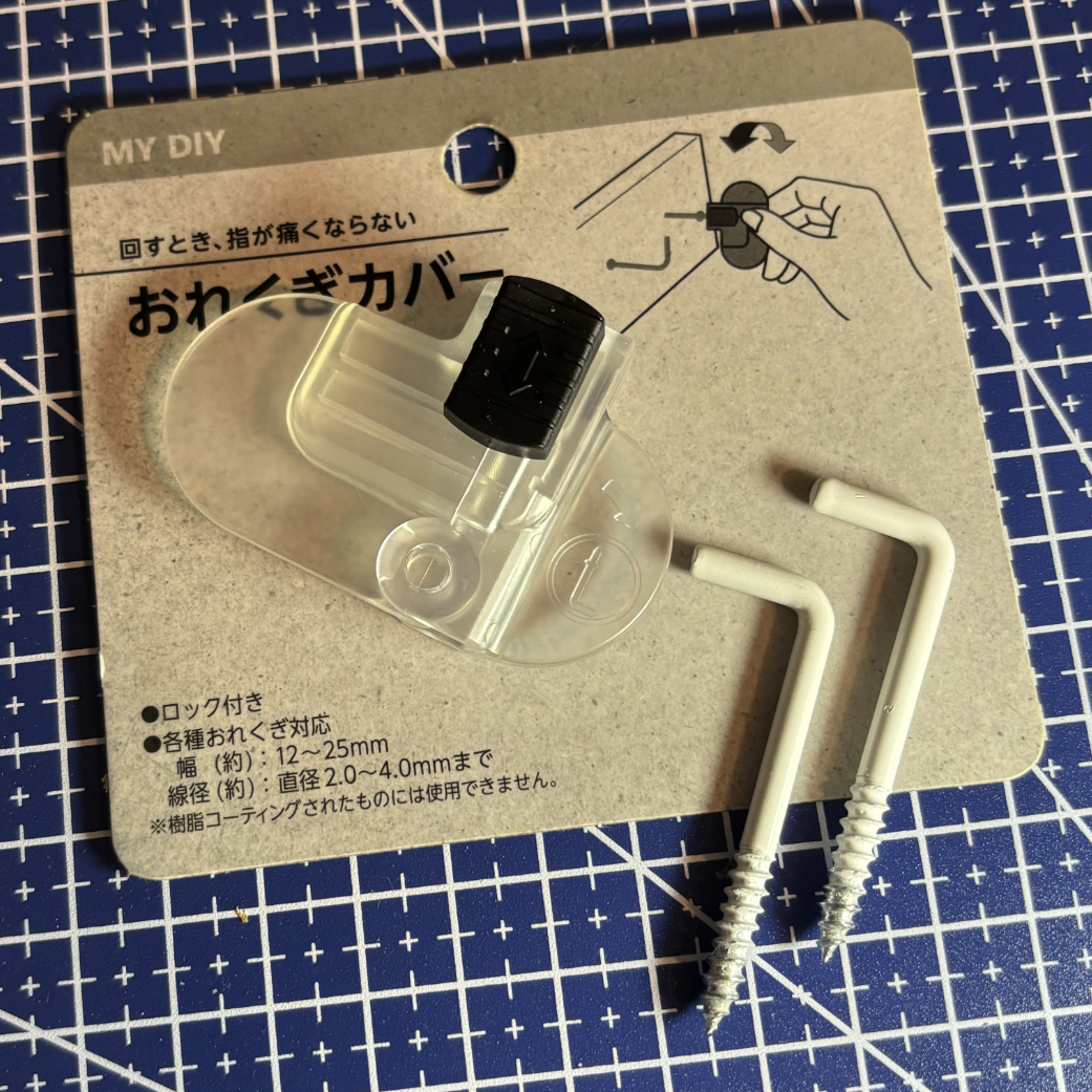 Foto de uma ferramenta em plástico translúcido, sobre um rótulo contendo desenho dela sendo usada para girar um parafuso em “L”, e texto em japonês. Ao lado dela, também aparecem na foto dois parafusos em “L”. 