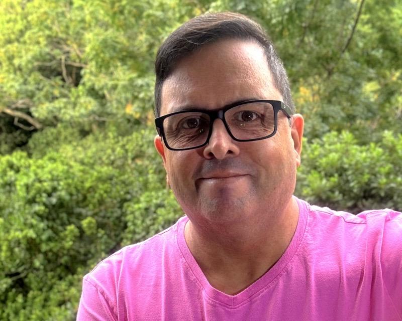 Foto minha olhando para a câmera, de camiseta cor de rosa e óculos, com a mata ao fundo